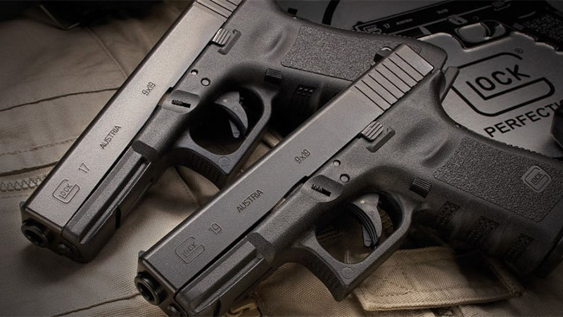 A Glock 17 and 19 gun lying on top of each other, set against a contrasting backdrop