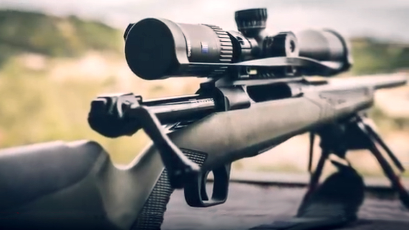 A partial image of a rifle in black color, with a scope attached