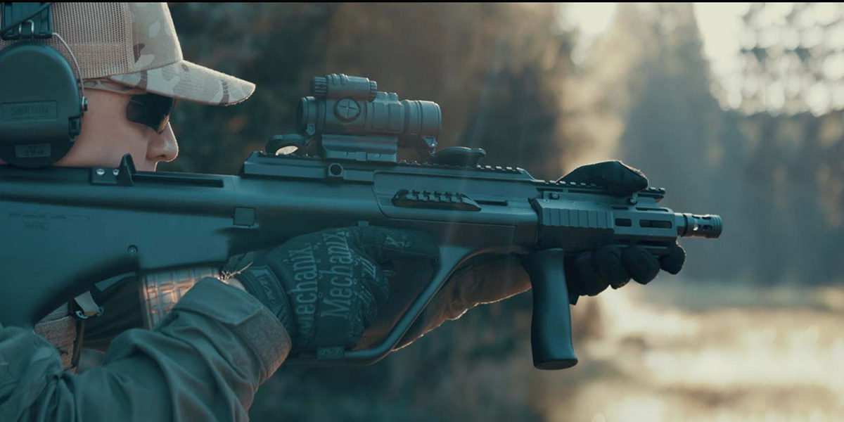 A man wearing a helmet stands confidently while holding an automatic rifle, ready for action